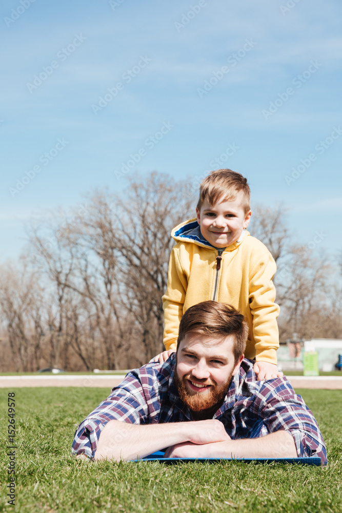 Bearded smiling father lies with little son in the park. Bearded smiling father lies with little son in the park.