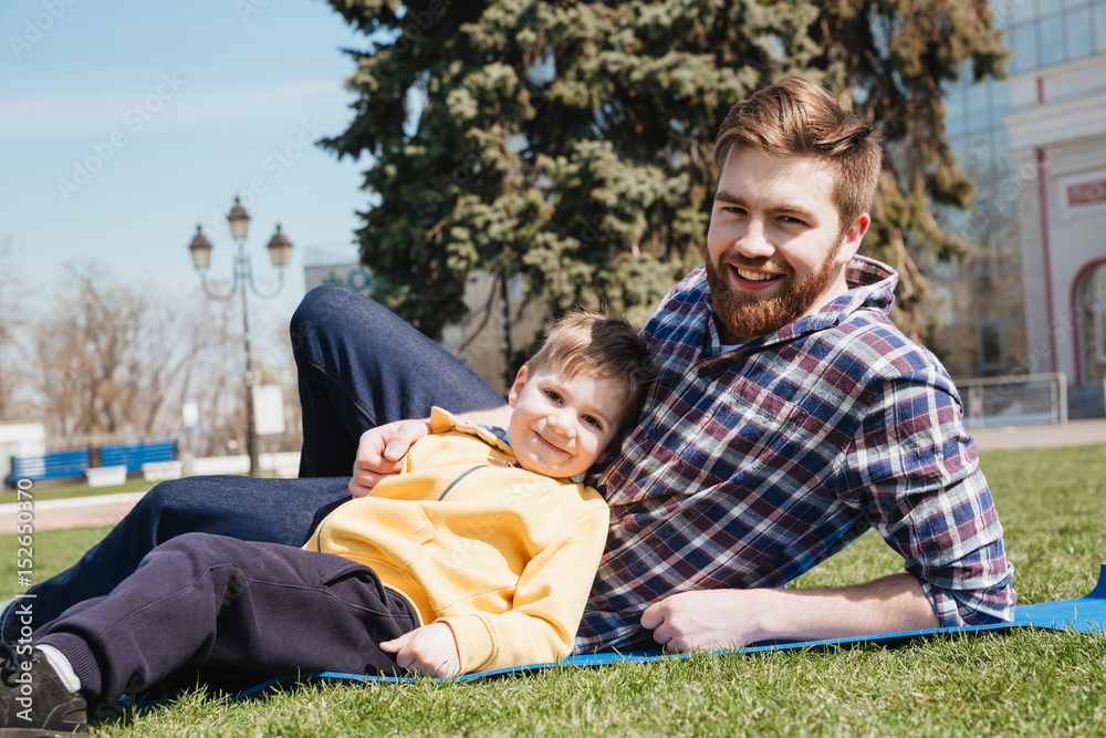 Fototapeta premium Bearded happy father lies outdoors with his son in park