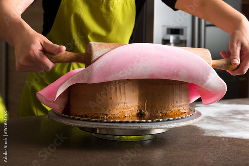 Close up of woman in bakery decorating heart shaped cake with pink royal icing photo