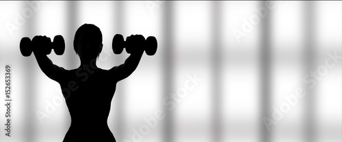 Silhouette of woman working out with dumbbells on a window background . photo