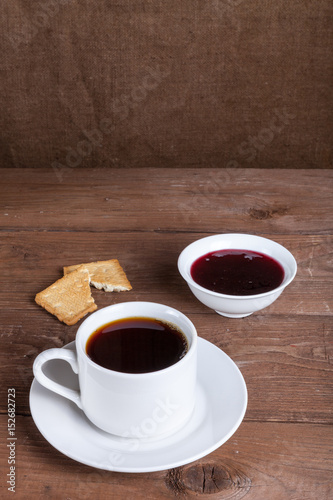 Cup of tea with jam and biscuits on old wooden table against the background of burlap