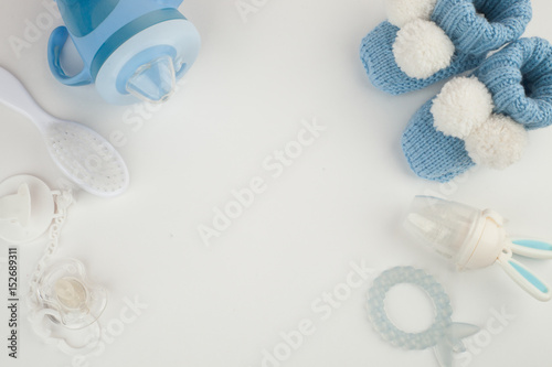 Baby boy accessories background: booties, tiny rod, soother, brush, and toys over white background with copy space; top view. Concept of Infancy and motherhood