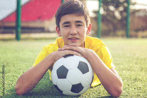 Asian boy teenager with a football ball lies on the grass. Sports, active way of life, game sports concept © olezzo