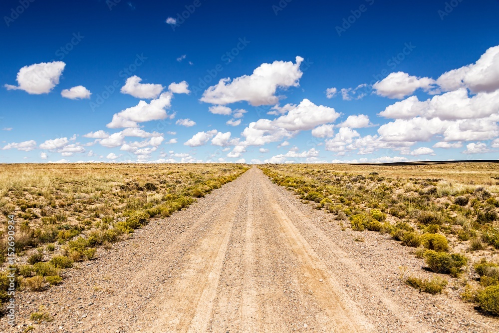 Naklejka premium lonelyness on infinite dirt road in the desert with clouds