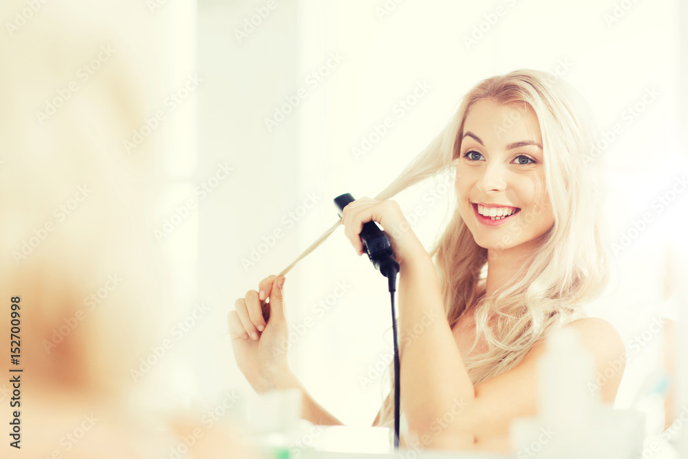 woman with styling iron doing her hair at bathroom woman with styling iron doing her hair at bathroom