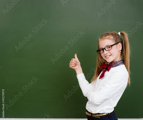 Teen girl standing near empty green chalkboard and showing thumbs up. Space for text