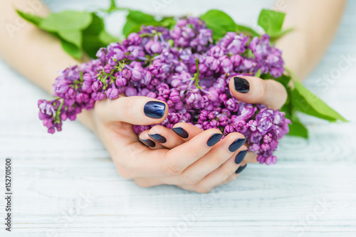 Woman cupped hands with beautiful dark blue manicure on fingernails holding lilac flowers