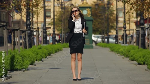 Young business lady calls on her mobile, while keeping a black file in a park