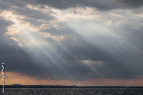 Sunrays at near sunset, with dark clouds in the background, an orange sky, and a lake below