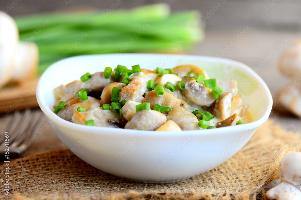 Fried mushrooms slices with sour cream and fresh green onions in a bowl. Healthy vegan meal. Home mushrooms recipe. Fresh mushrooms, green onions, burlap textile on vintage wooden table Fried mushrooms slices with sour cream and fresh green onions in a bowl. Healthy vegan meal. Home mushrooms recipe. Fresh mushrooms, green onions, burlap textile on vintage wooden table