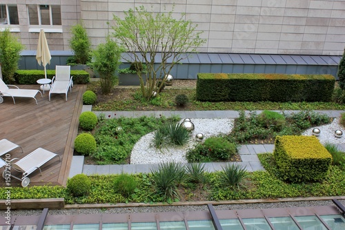 Roof garden with green plants and silver which balls and wooden terrace with rest chairs