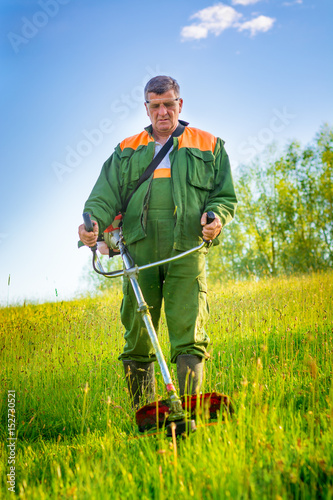 worker cutting grass in garden with the weed trimmer