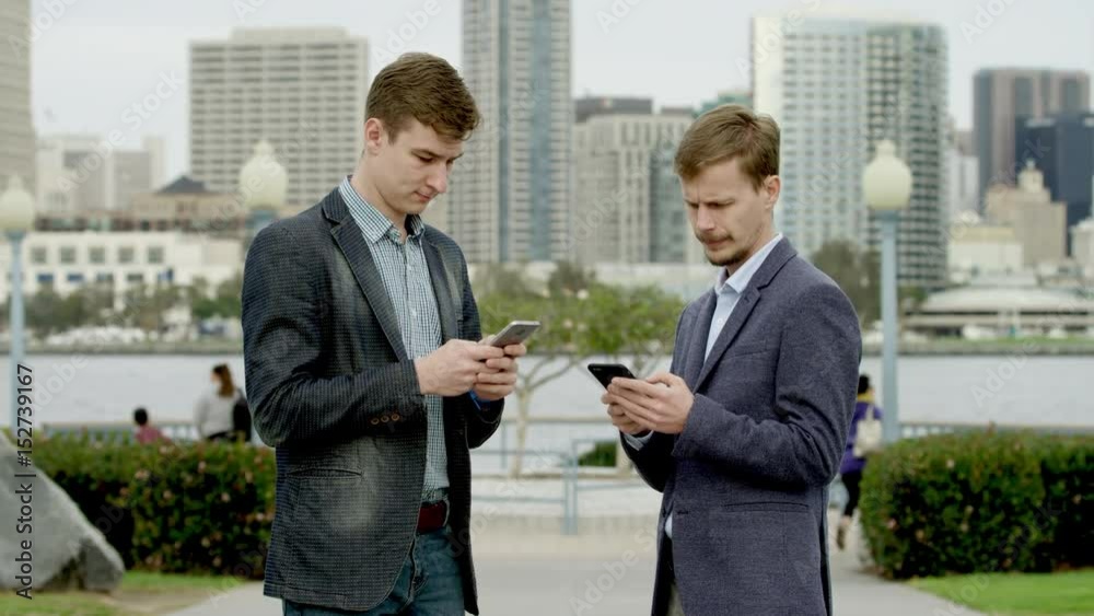 Two businessmen are standing on a street with their smartphones Two businessmen are standing on a street with their smartphones