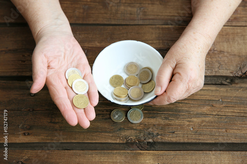 Картината върху платно Hands of senior woman with bowl and coins on wooden background