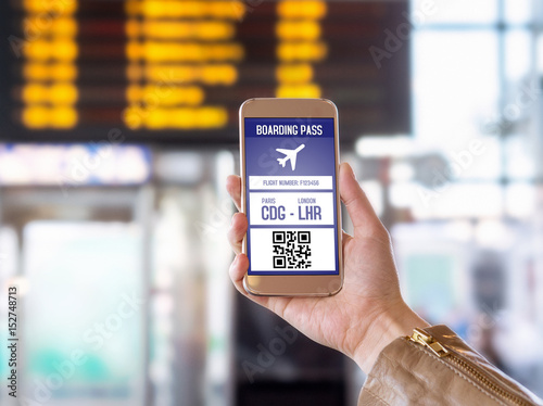 Boarding pass in mobile phone. Woman holding smartphone in airport with modern ticket on screen. Easy and fast access to aeroplane. Terminal and timetable in the blurred background. 