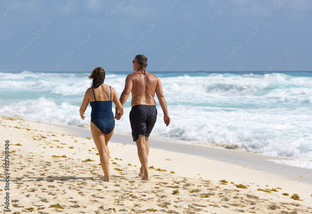 Adult couple walking down the beach on a sunny day. The shore of the Caribbean sea. Vacation concept image for lovers and married people.