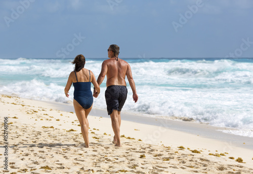 Adult couple walking down the beach on a sunny day. The shore of the Caribbean sea. Vacation concept image for lovers and married people.