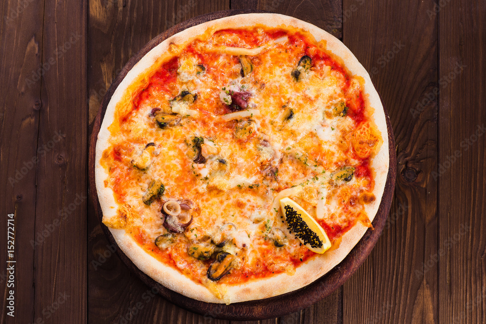 delicious Italian seafood pizza on a dark wooden table (close top view).