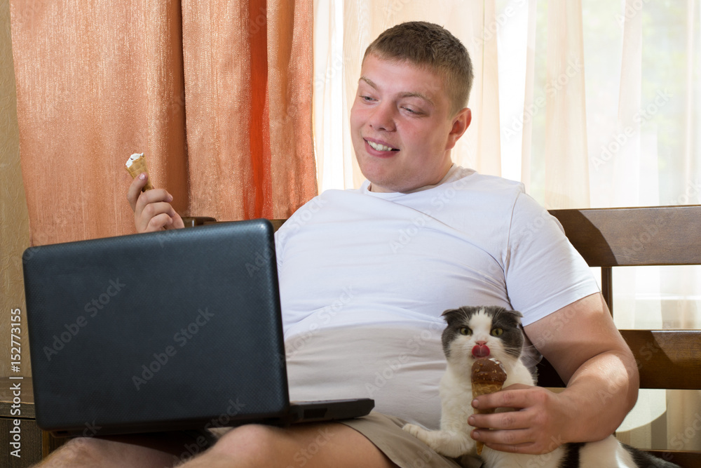 Man with laptop and funny cat eating ice cream cone in the bed Man with laptop and funny cat eating ice cream cone in the bed