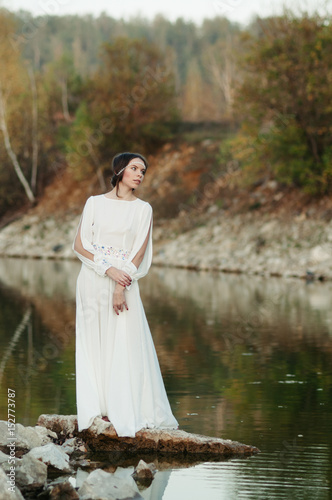 A girl in a white dress on the shore of a pond