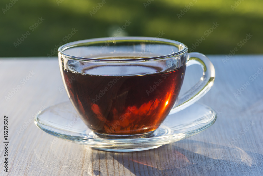 tea time/transparent sunny cup of tea on light wooden table outdtoors tea time/transparent sunny cup of tea on light wooden table outdtoors