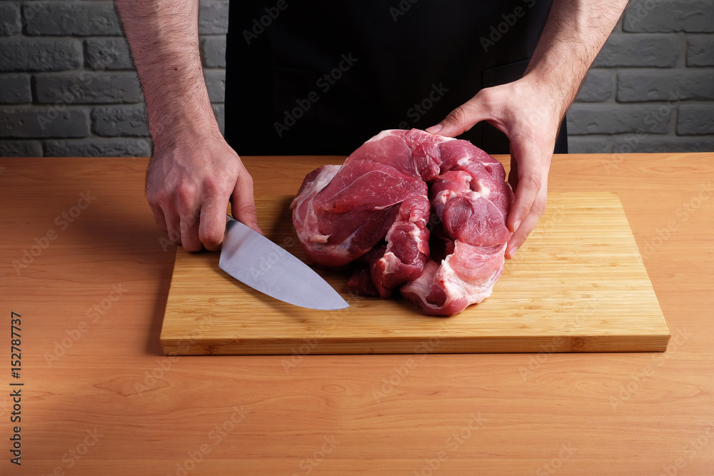 man in the apron cuts of pork or beef on a cutting wooden board