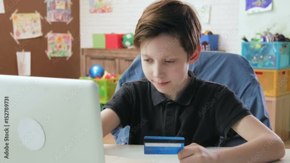 Cute little boy shopping online using entering credit card number using laptop computer and is happy after making a purchase Cute little boy shopping online using entering credit card number using laptop computer and is happy after making a purchase