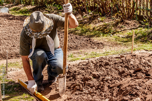 the farmer prepares the place for the greenhouse using a level and a shovel photo