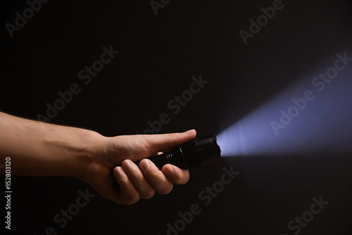 Male hand holding a led flashlight with a wide white beam on a black background, leaving the left side of the frame