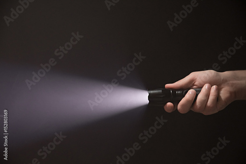 Male hand holding a led flashlight with a wide white beam on a black background, leaving the right side of the frame