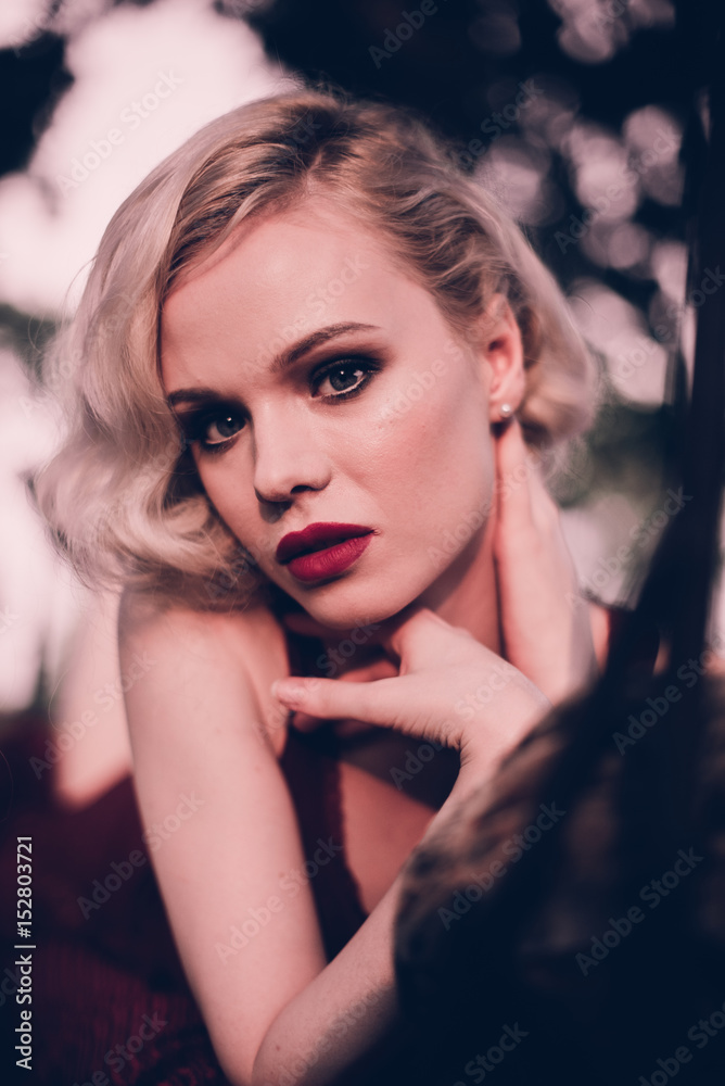 Beautiful and elegant blonde woman with red lips and hair waves wearing wine red nightie posing on the bed outdoors autumn, retro vintage style and fashion. Beautiful and elegant blonde woman with red lips and hair waves wearing wine red nightie posing on the bed outdoors autumn, retro vintage style and fashion.
