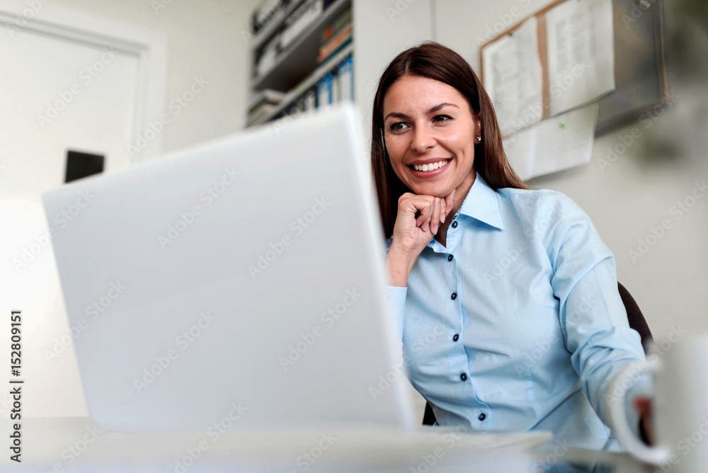 Smiling businesswoman in office working on laptop computer Smiling businesswoman in office working on laptop computer
