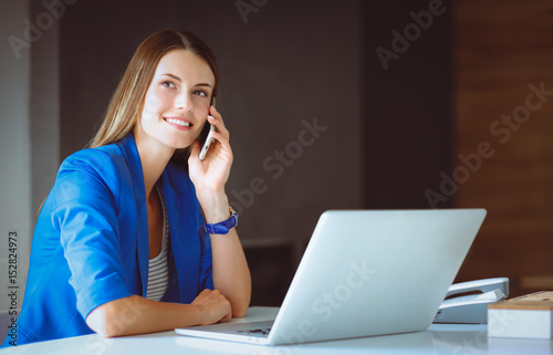 Portrait of a young woman on phone in front of a laptop computer photo