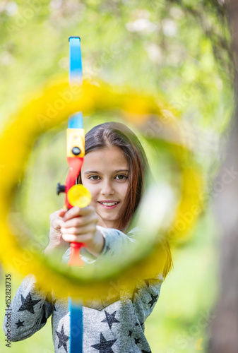 Young girl archer with bow aiming through flower wreath