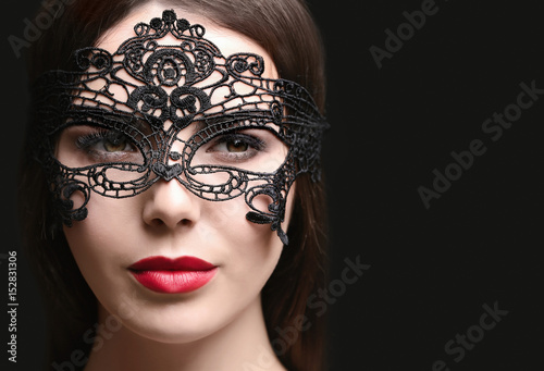 Beautiful young woman in mask on black background