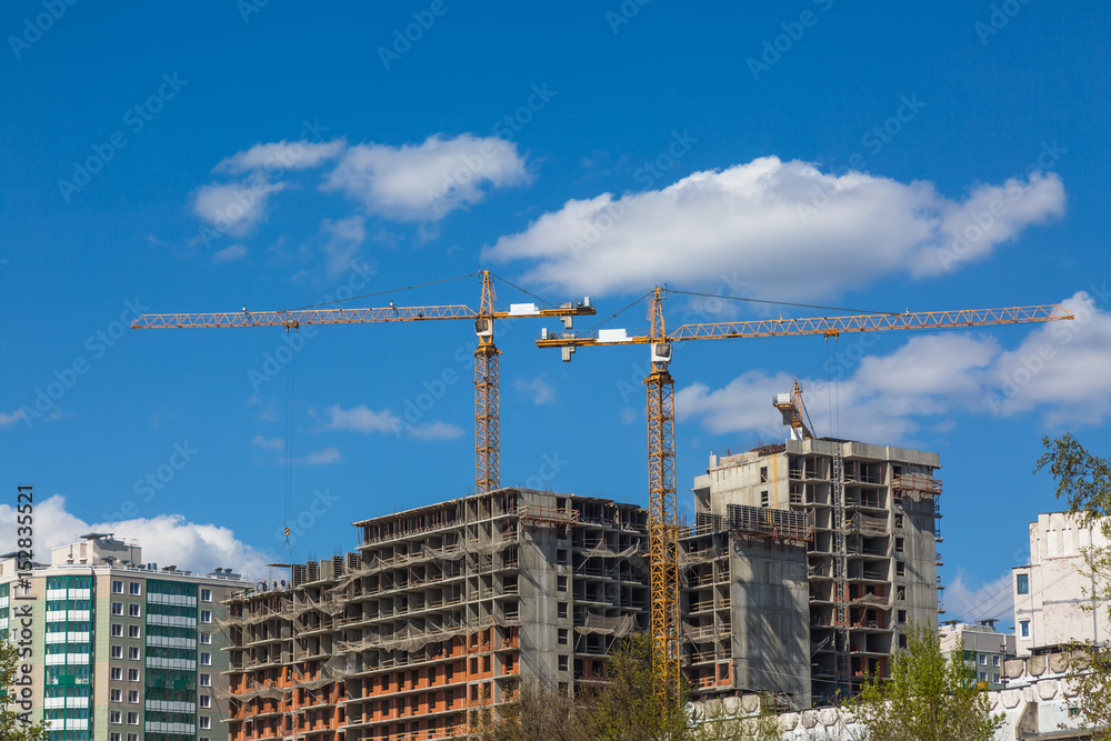 Hoisting cranes and house construction with blue sky and clouds