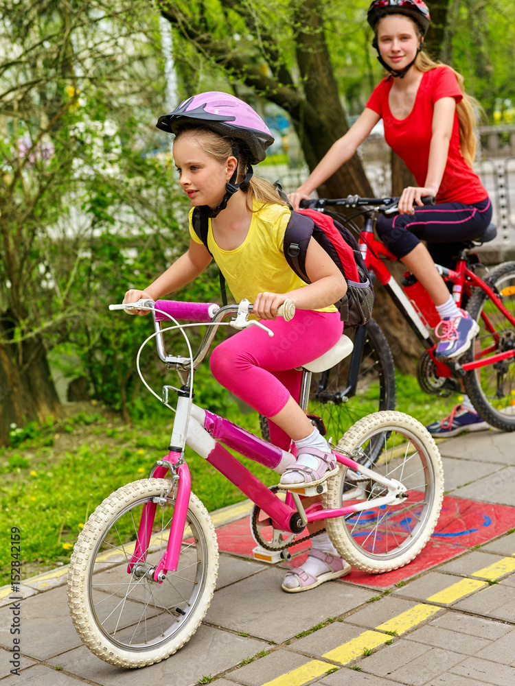 Obraz premium Bicycle path and sign with children. Girls wearing helmet with rucksack ciclyng ride. Kids are on yellow bike lane. Alternative to urban transport. Sisters compete in speed for cycling.