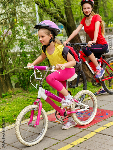 Bicycle path and sign with children. Girls wearing helmet with rucksack ciclyng ride. Kids are on yellow bike lane. Alternative to urban transport. Sisters compete in speed for cycling.