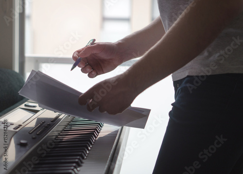 Musician brainstorming and innovating new song ideas at piano by the window. Composer writing notes to paper or planning arrangement. Man come up with pop lyrics. Inspiration and creativity concept. photo