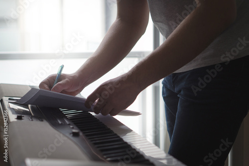 Composer and songwriter writing notes or lyrics on paper on piano. Musician write a song in home studio on an digital instrument. Excited about new idea or melody. Shadowy dark ambient lightning.  photo