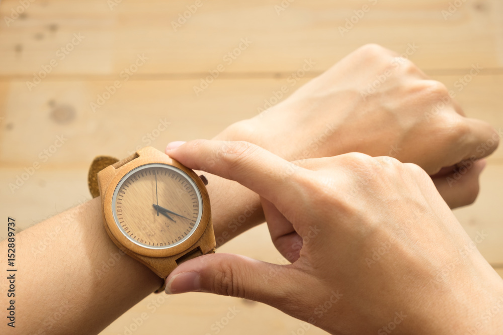 top view. young woman equip wooden wrist watch on her arm and checking time. wooden are background. this image for equipment,accessory and fashion concept top view. young woman equip wooden wrist watch on her arm and checking time. wooden are background. this image for equipment,accessory and fashion concept