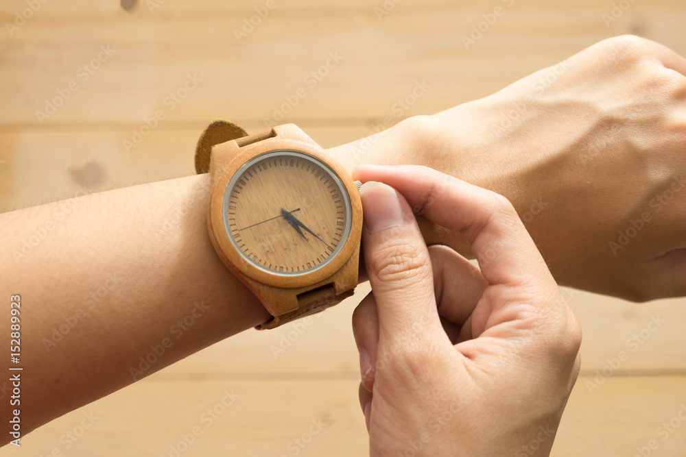 top view. young woman equip wooden wrist watch on her arm and checking time. wooden are background. this image for equipment,accessory and fashion concept top view. young woman equip wooden wrist watch on her arm and checking time. wooden are background. this image for equipment,accessory and fashion concept