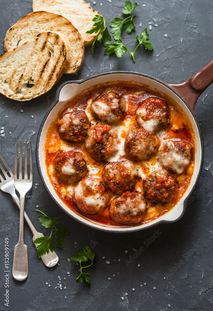 Baked pork meatballs with mozzarella and tomato sauce in a frying pan on a dark background, top view