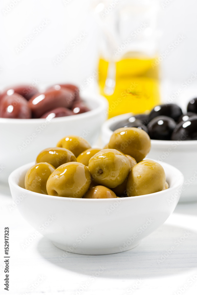 assortment of different kinds of organic olives on white table, vertical closeup assortment of different kinds of organic olives on white table, vertical closeup