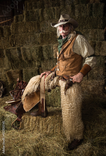 Slika na platnu Old west cowboy with woolie chaps, pistols, vest and cowboy hat full length port