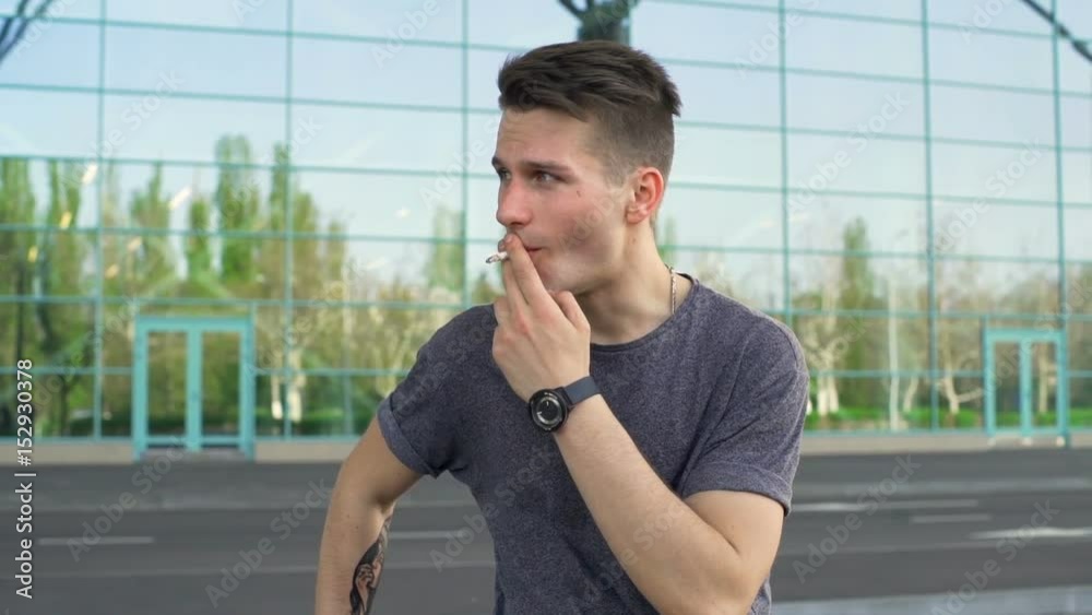 Young man looking away and smoking a cigarette slow motion