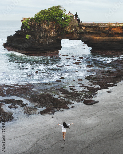 Happy woman running by empty Batu Bolong beach near holy balinese temple Tanah Lot. Nobody around in the morning. Freedom and joy. Sacred pura for local indonesian people