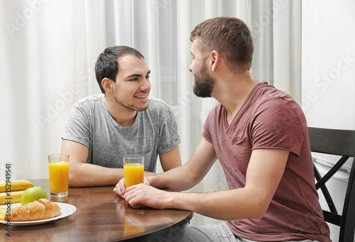 Happy gay couple having breakfast in kitchen