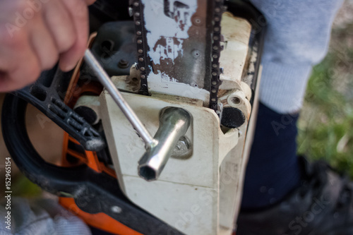 Woodman made a stop in the cutting of trees to sharpen and tighten the chain of chainsaws, hand with screwdriver