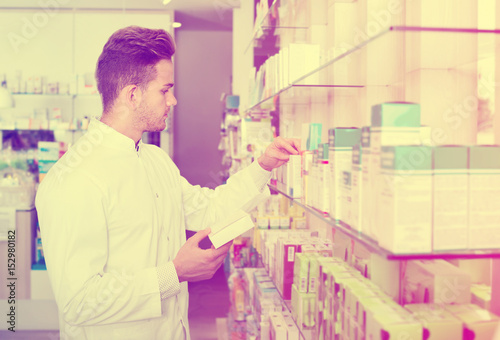 Male pharmacist wearing white coat standing  in drug store